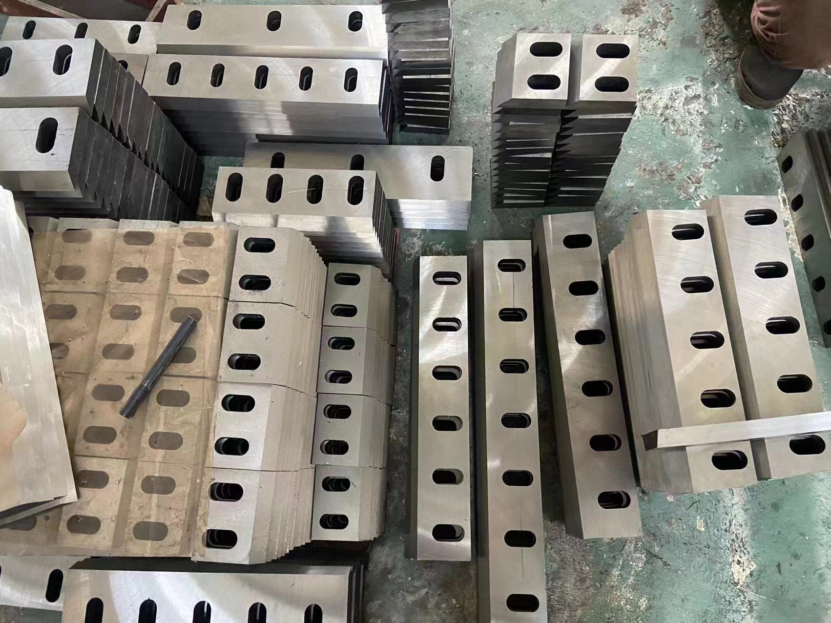 Bulk stock of industrial plastic crusher blades and rotor stator knives stacked in a manufacturing factory