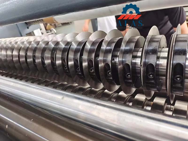 Multiple alloy steel rotary slitter knives running synchronously on an automated corrugated board slitting machinery spindle arbor.