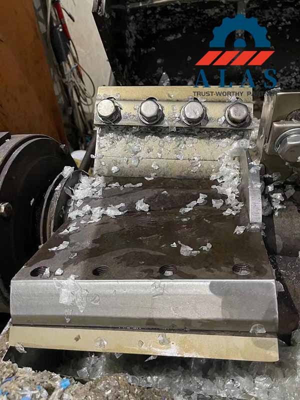 Industrial crushing chamber processing clear post-consumer PET bottles flakes with synchronized flat rotary and stationary knives combination.
