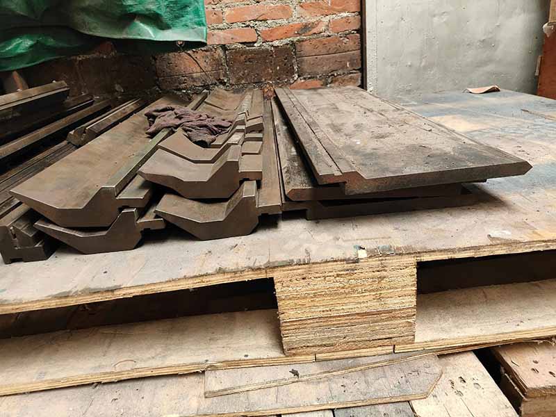 A pile of worn-out conventional press brake punches and lower dies stacked on a wooden pallet inside a fabrication shop.