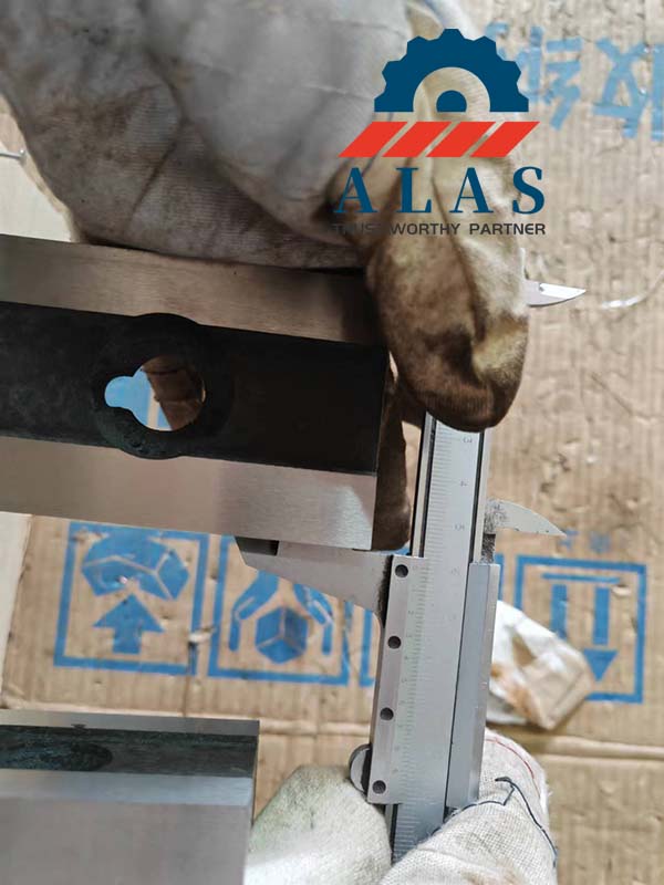 Quality control inspector measuring custom shear blade thickness with vernier caliper