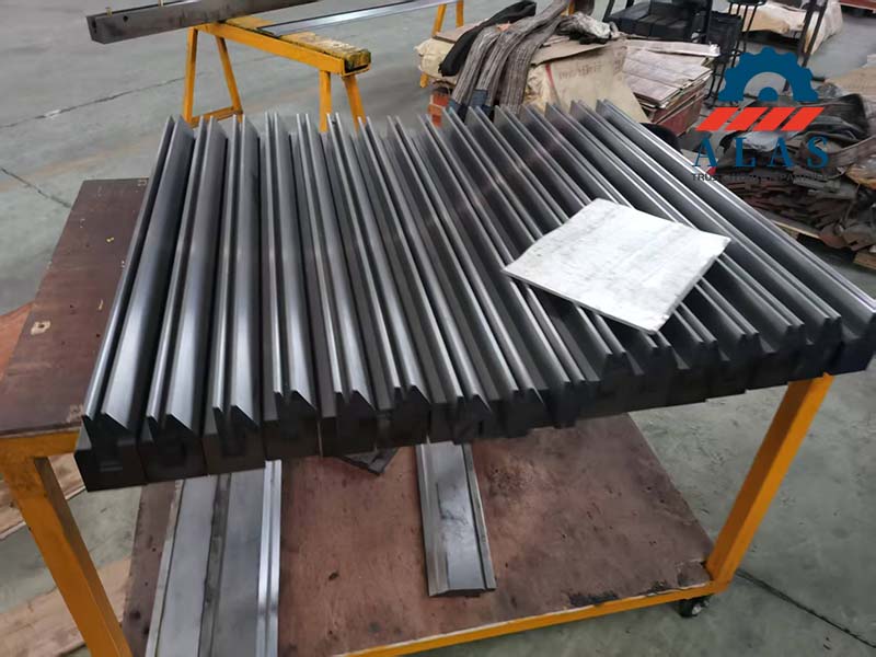 A large batch of precision ground segmented and full-length press brake hemming tools stacked neatly on a workshop rack with production sheets.