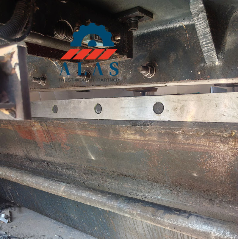 Segmented tool steel blade bolted perfectly onto the upper pivoting machine ram seat of an industrial hydraulic swing beam shearing machine.