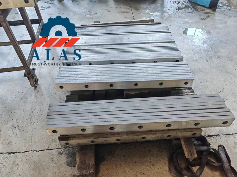 Multiple batches of finished heavy duty shearing machine blades in various thicknesses stacked in a metal workshop
