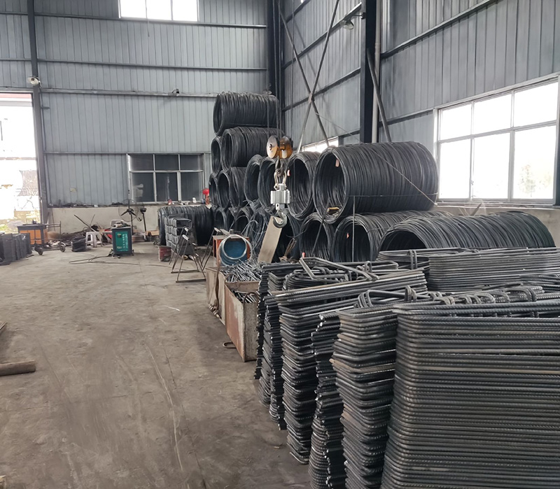 Bent steel rebar components and wire rod coils inside an industrial reinforcement fabrication workshop