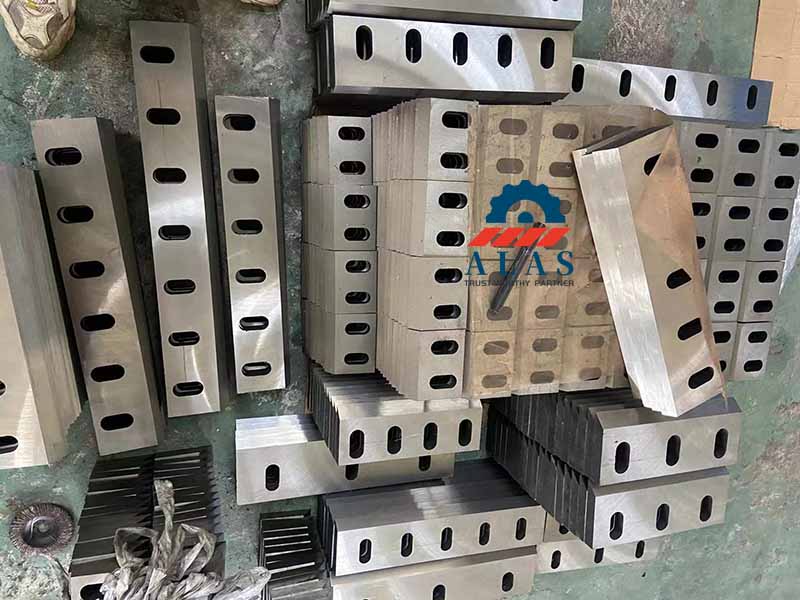A massive factory wholesale stock inventory of multi-hole flat crusher blades and bed counter-knives stacked on the workshop floor.